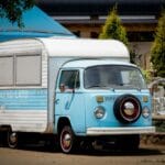 Niebieski zabytkowy food truck z przyczepą zaparkowany przy fontannie