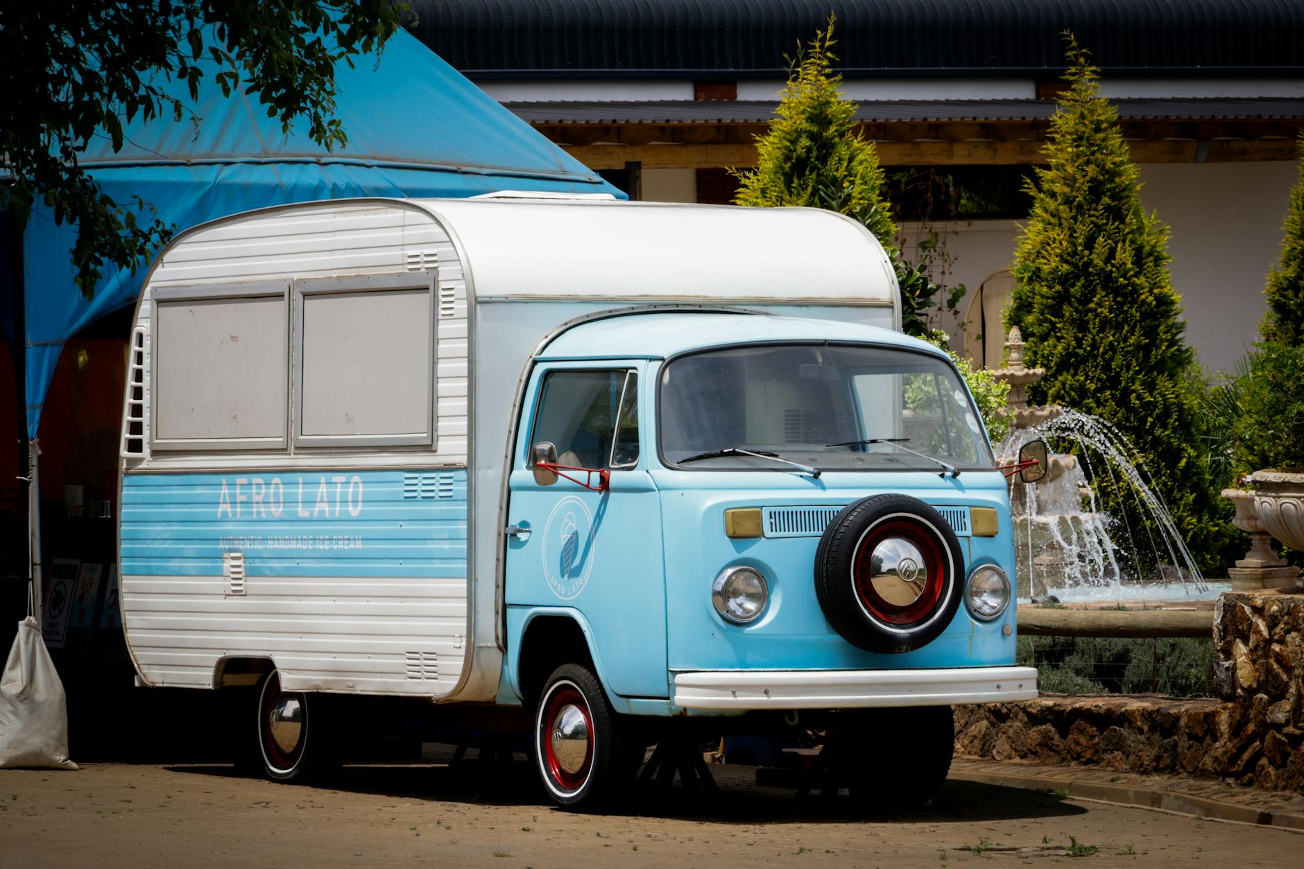 Niebieski zabytkowy food truck z przyczepą zaparkowany przy fontannie