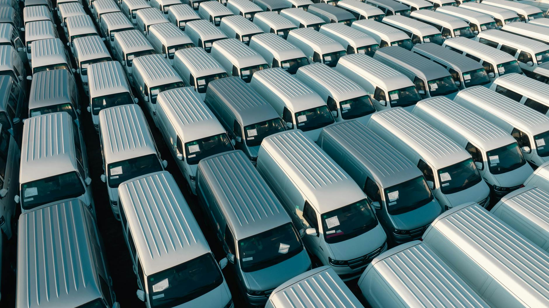 Białe busy firmowe zaparkowane rzędami na placu transportowym