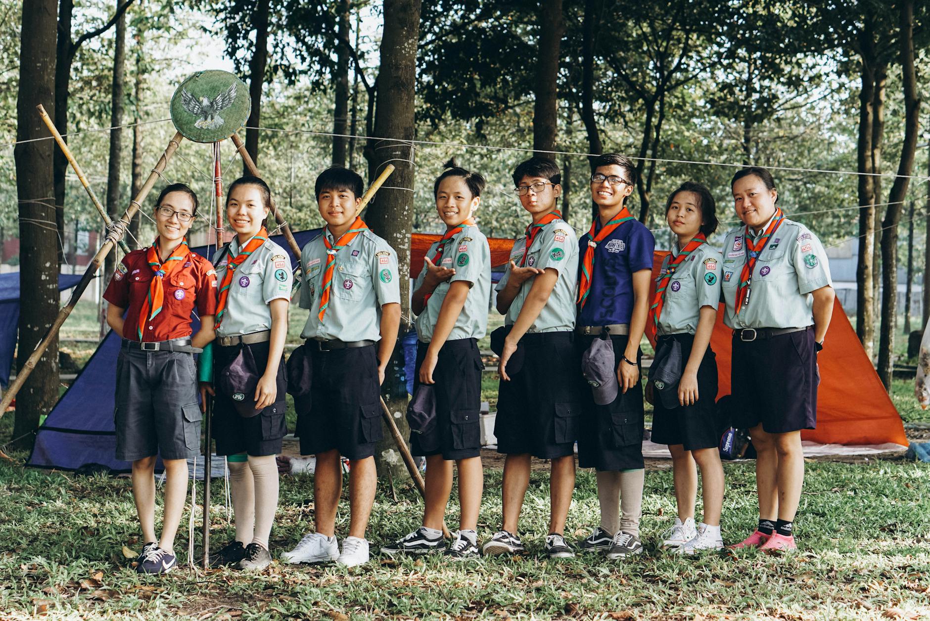 Grupa uśmiechniętych harcerzy w mundurach pozuje na biwaku w lesie