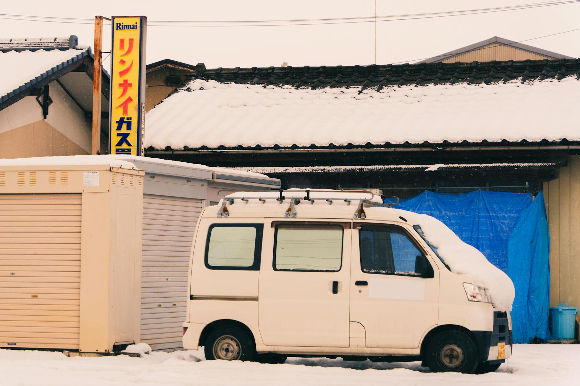Mały bus zasypany śniegiem przed tradycyjnym japońskim domem zimą