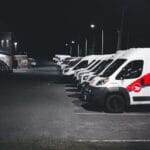 Białe i czerwone auta dostawcze zaparkowane nocą na oświetlonym parkingu