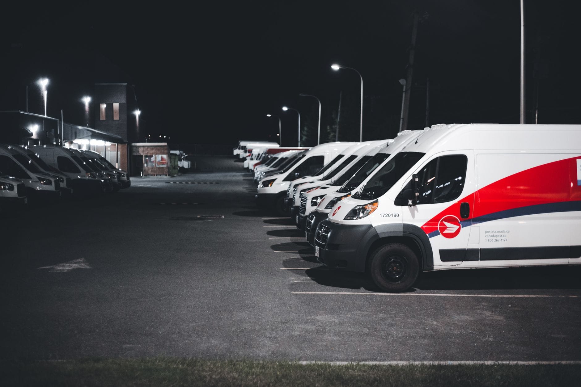 Białe i czerwone auta dostawcze zaparkowane nocą na oświetlonym parkingu