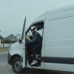 Kurier wyjmuje paczkę z busa w spokojnej dzielnicy domów jednorodzinnych