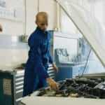 Mechanik w niebieskim kombinezonie sprawdza silnik auta dostawczego w warsztacie