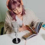 Młoda kobieta nagrywa podcast o książkach przy biurku z mikrofonem