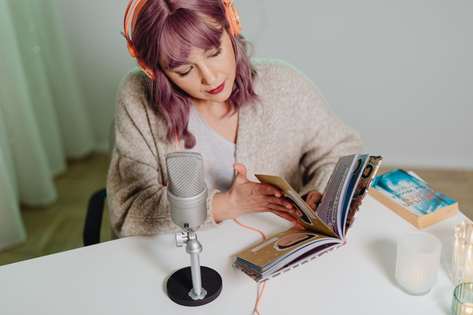 Młoda kobieta nagrywa podcast o książkach przy biurku z mikrofonem